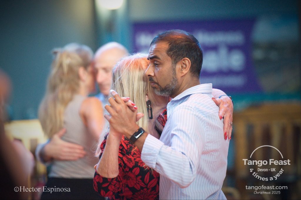Atul Rana dancing Argentine Tango at Tango Feast in Devon. Photo shows a tango embrace with Atul and a female dancer in red.